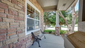A covered porch with two benches, a brick wall, and a window with blinds. - Pet-Friendly Meridian Vacation Rental w/ Fire Pit! (Meridian)