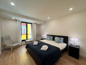 A hotel room with a bed, two bedside tables, a chair, and a window with curtains. - Faro Design 4 by Homing (Faro)