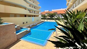 A swimming pool with lounge chairs, a brick wall, and a multi-story building with balconies. - Vilamoura Central 2 With Pool by Homing (Loulé)