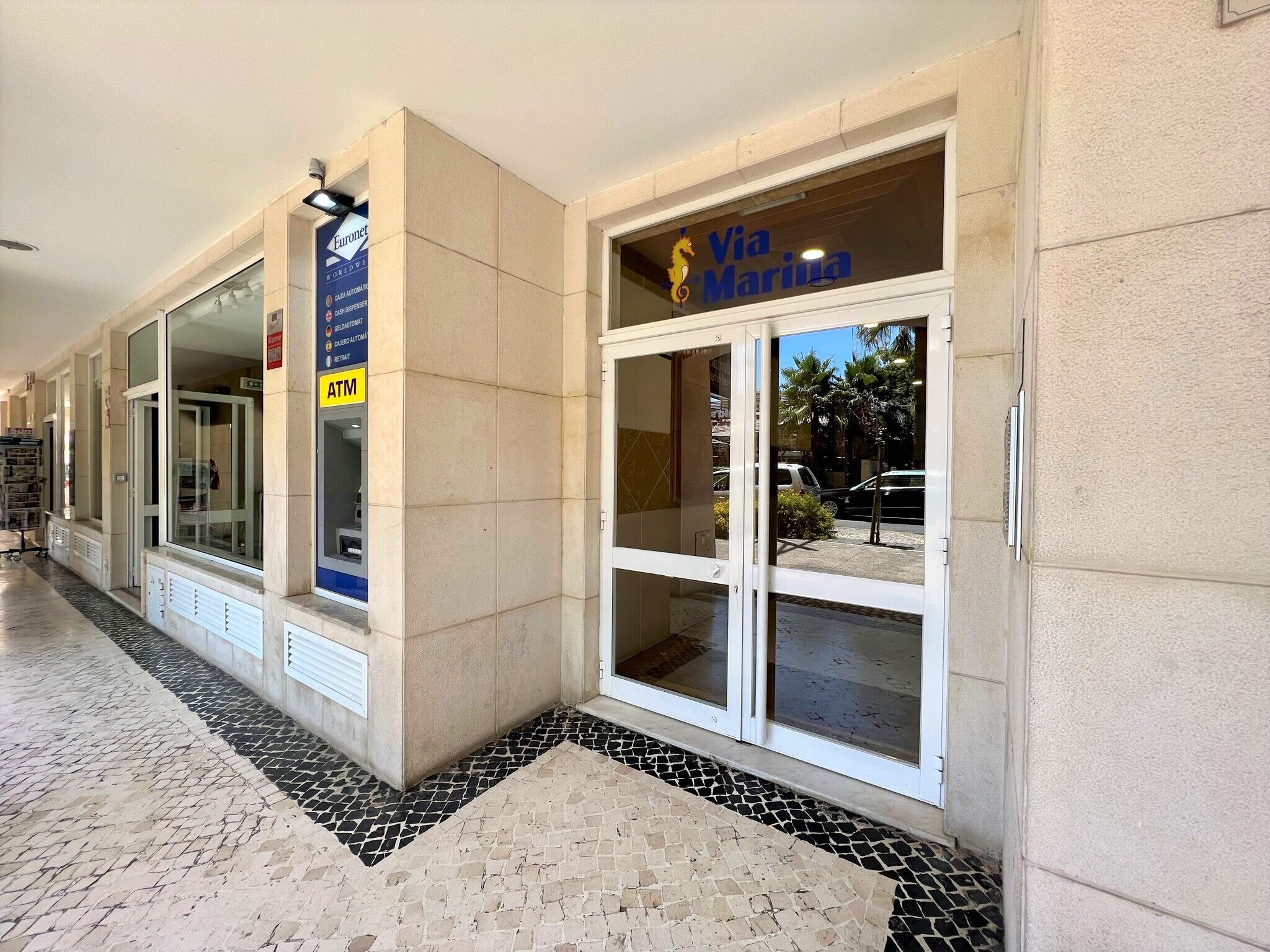 A corridor with a Via Marina sign, an ATM, and a Furonet store.