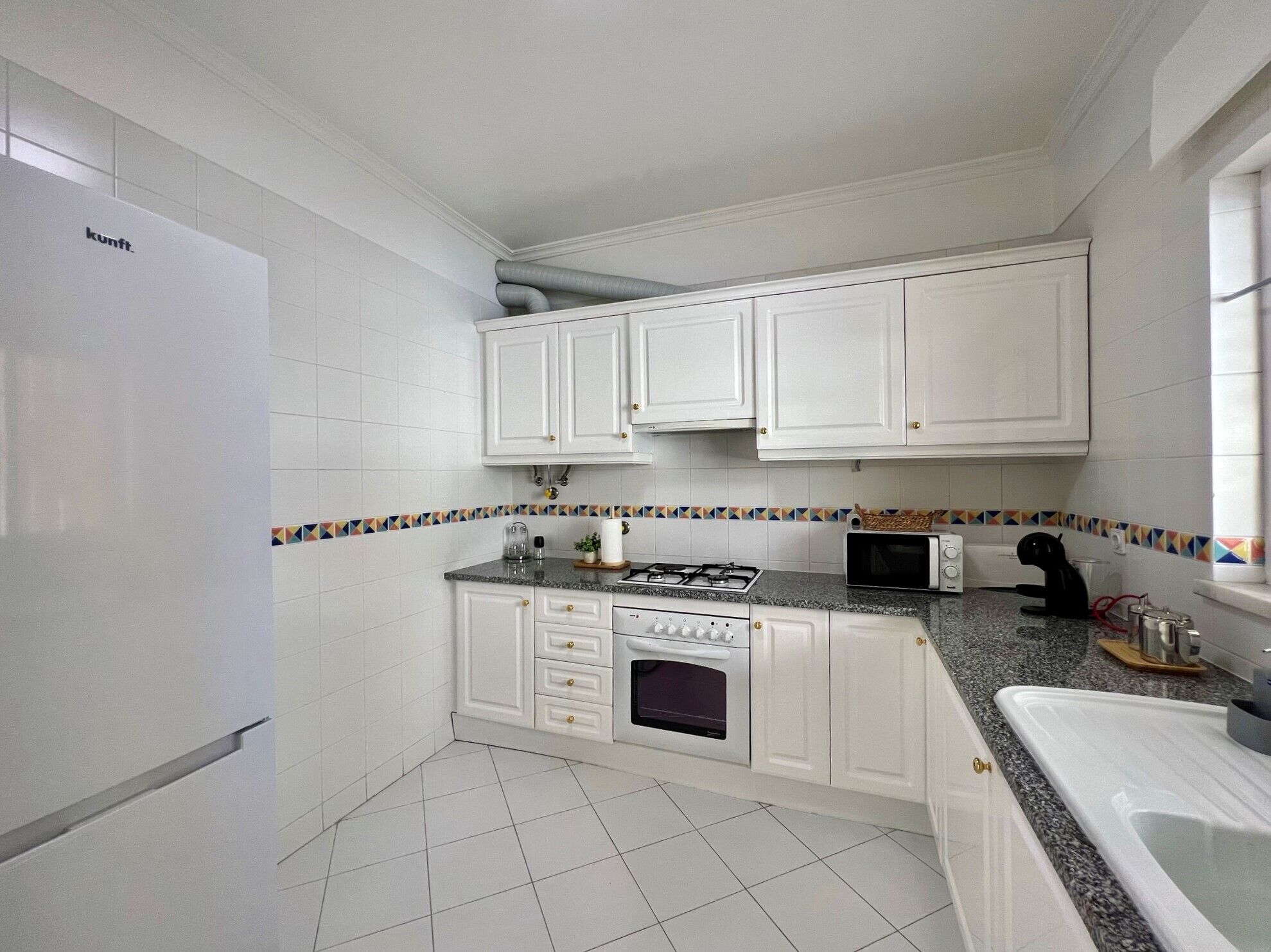 Een keuken met witte kastjes, een gasfornuis, een oven, een magnetron en een spoelbak.