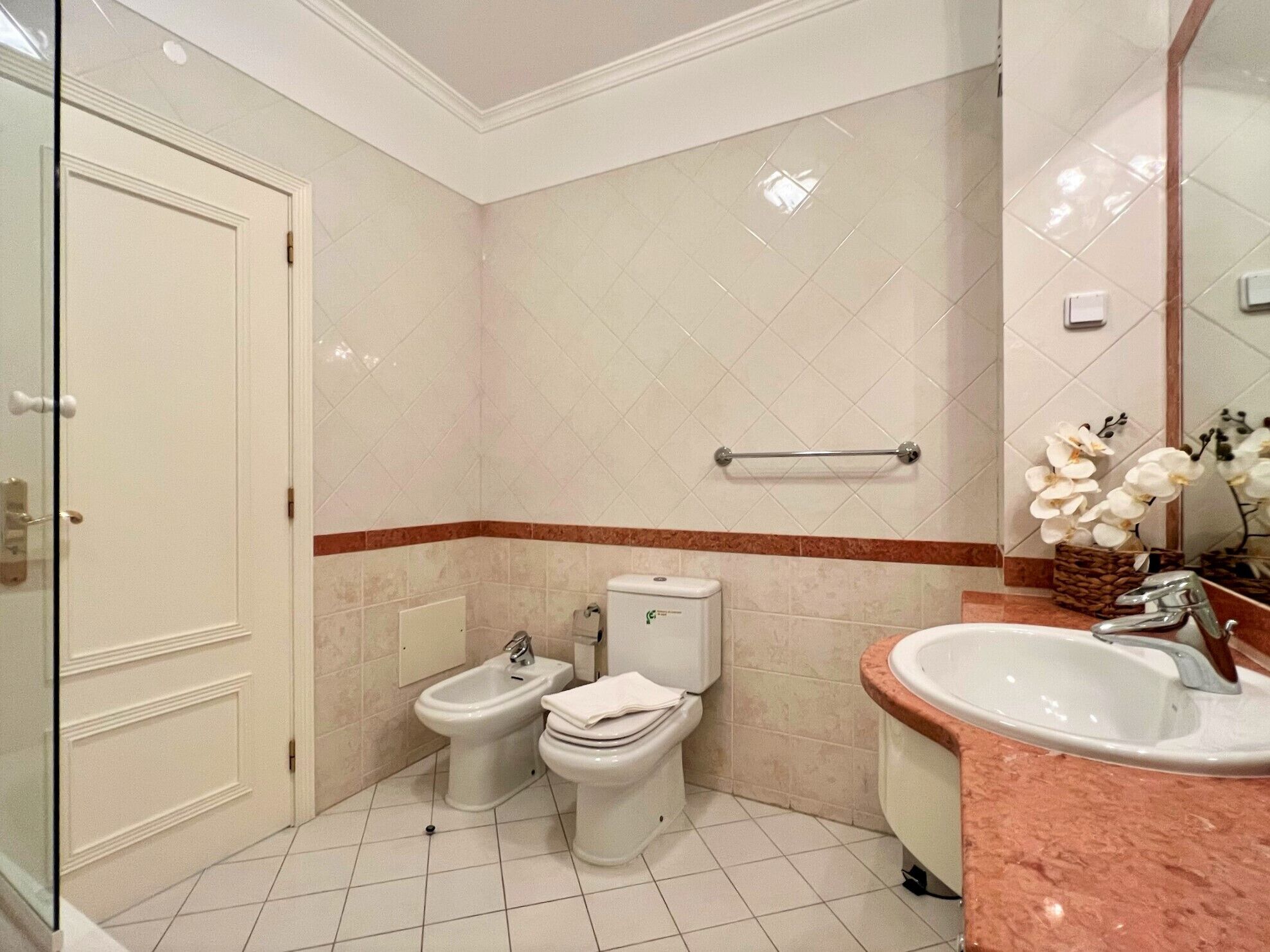 A bathroom with a toilet, bidet, and sink, with a mirror and a towel rack.