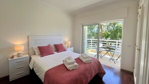A bedroom with a bed, two bedside lamps, a nightstand, a dresser, and a balcony with a table and chairs. - Vilamoura Central 2 With Pool by Homing (Loulé)