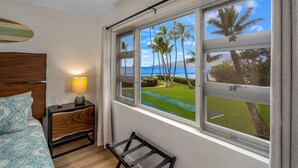 A bedroom with a bed, bedside table, lamp, and a window with a view of palm trees and a golf course.