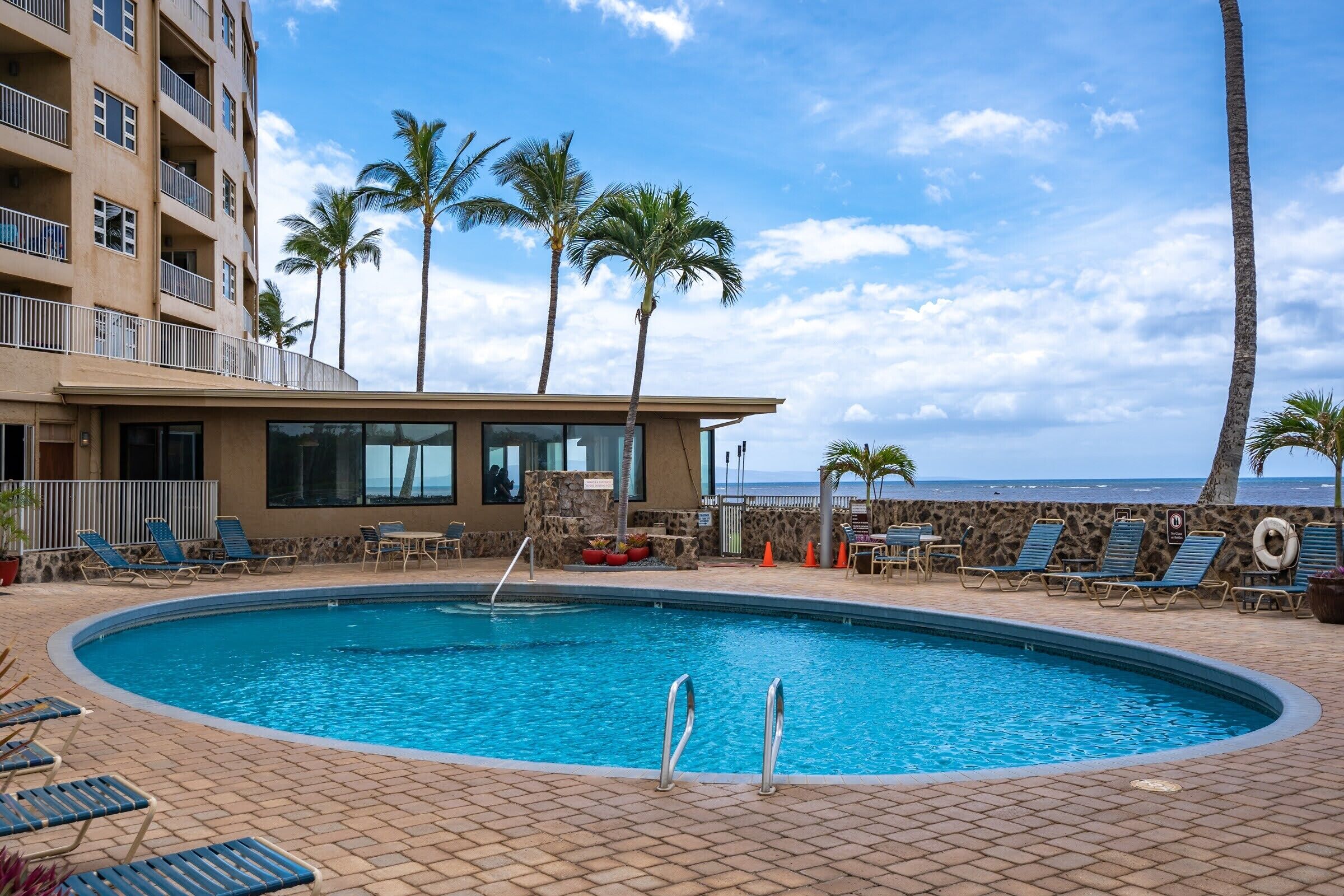 A swimming pool with lounge chairs, palm trees, and a building with balconies.
