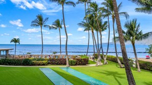 A scenic view of a courtyard with a shuffleboard court, palm trees, and a beach in the background.