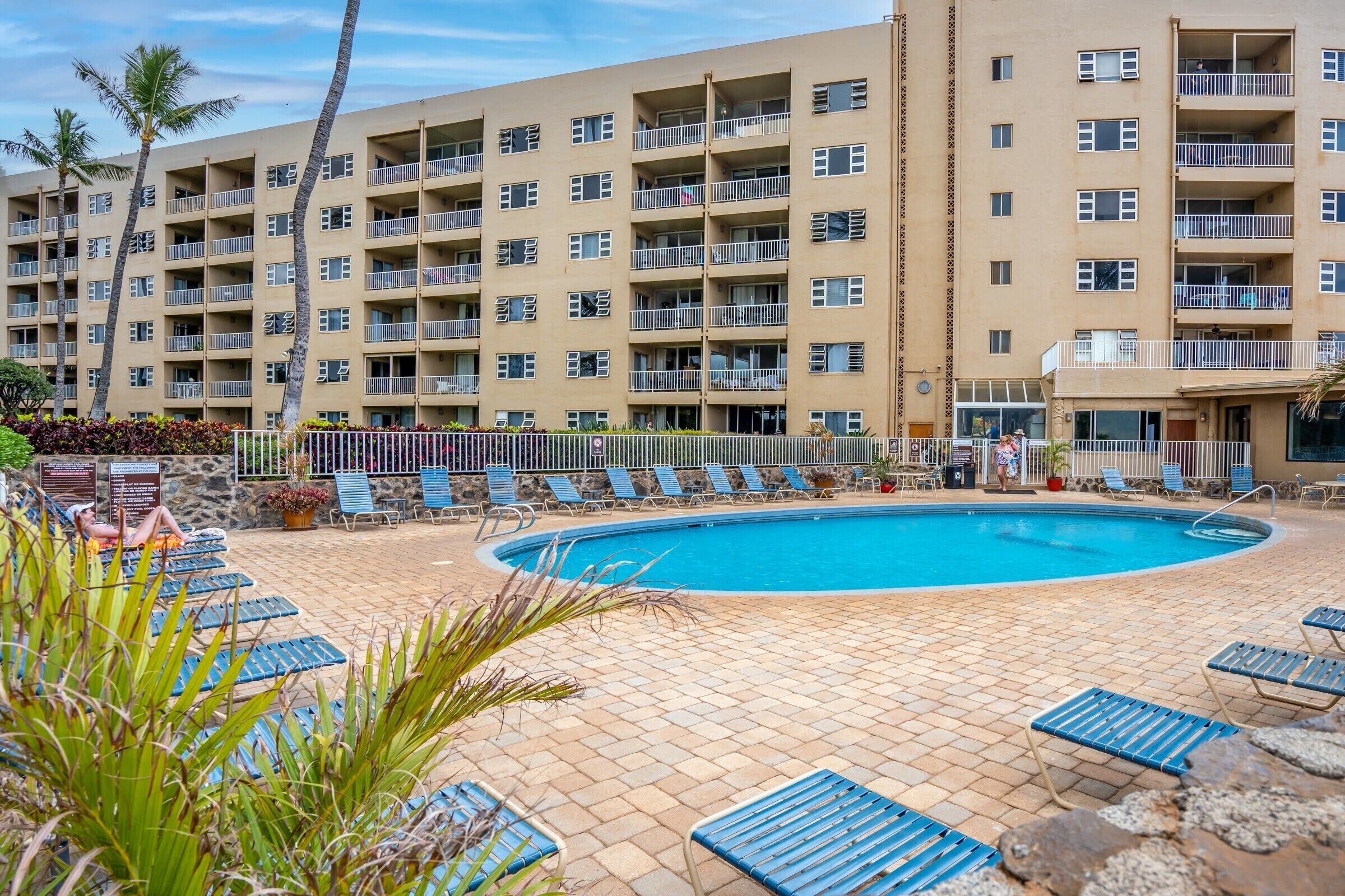 A hotel with a swimming pool surrounded by lounge chairs and palm trees.
