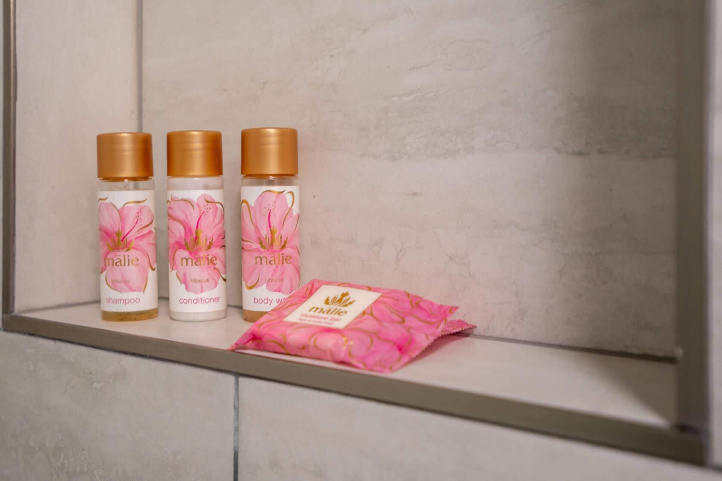 Three bottles of Malie body wash and conditioner on a shelf.