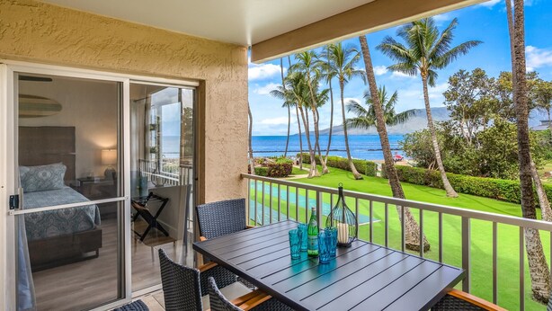 A balcony with a table, chairs, and a view of the ocean and palm trees.