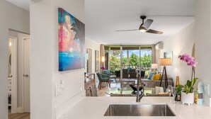 A modern kitchen with a large island, a dining area with a glass table, and a view of the outdoors.