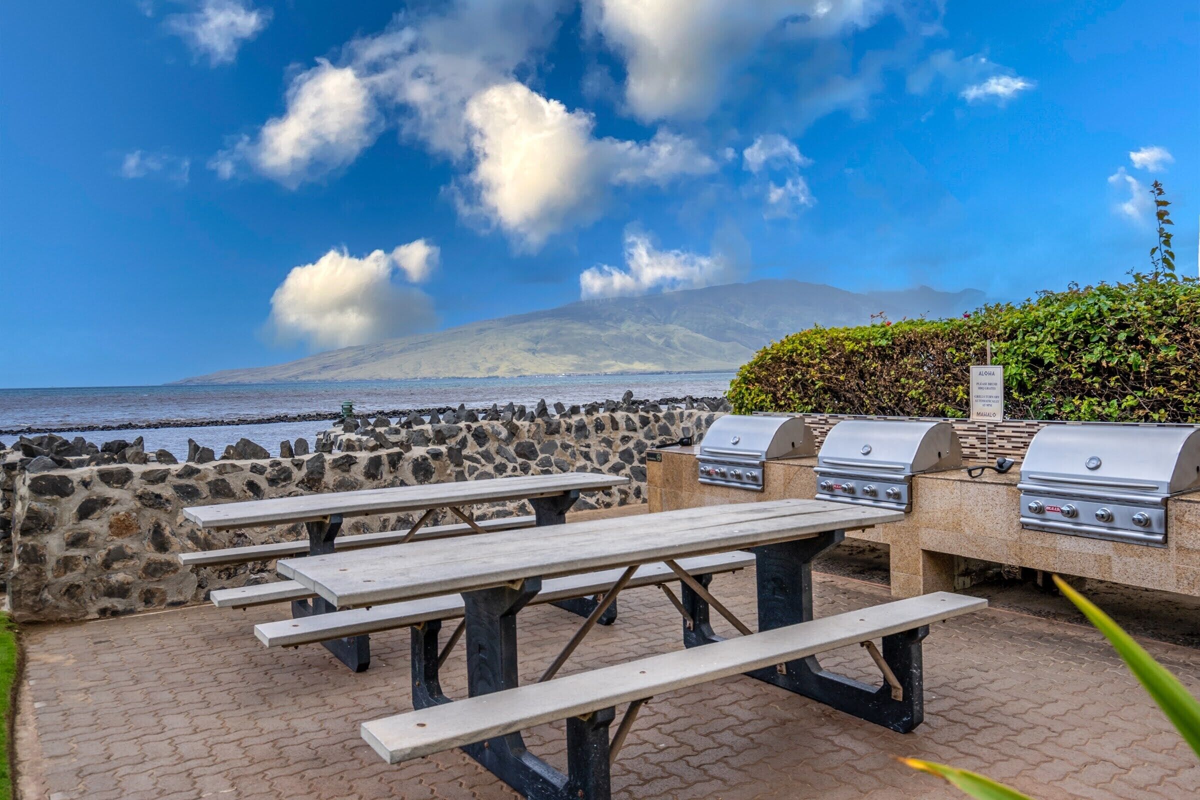 An outdoor dining area with stone walls, picnic tables, and barbecue grills.