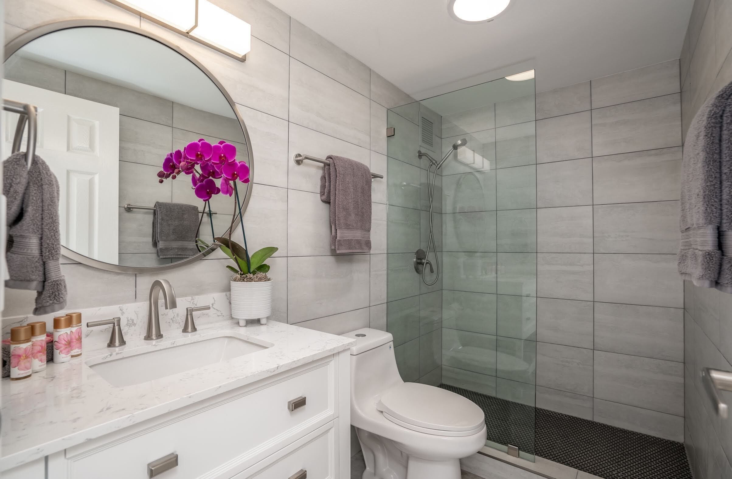 A modern bathroom with a glass-enclosed shower, a white sink with a marble countertop, and a potted orchid.