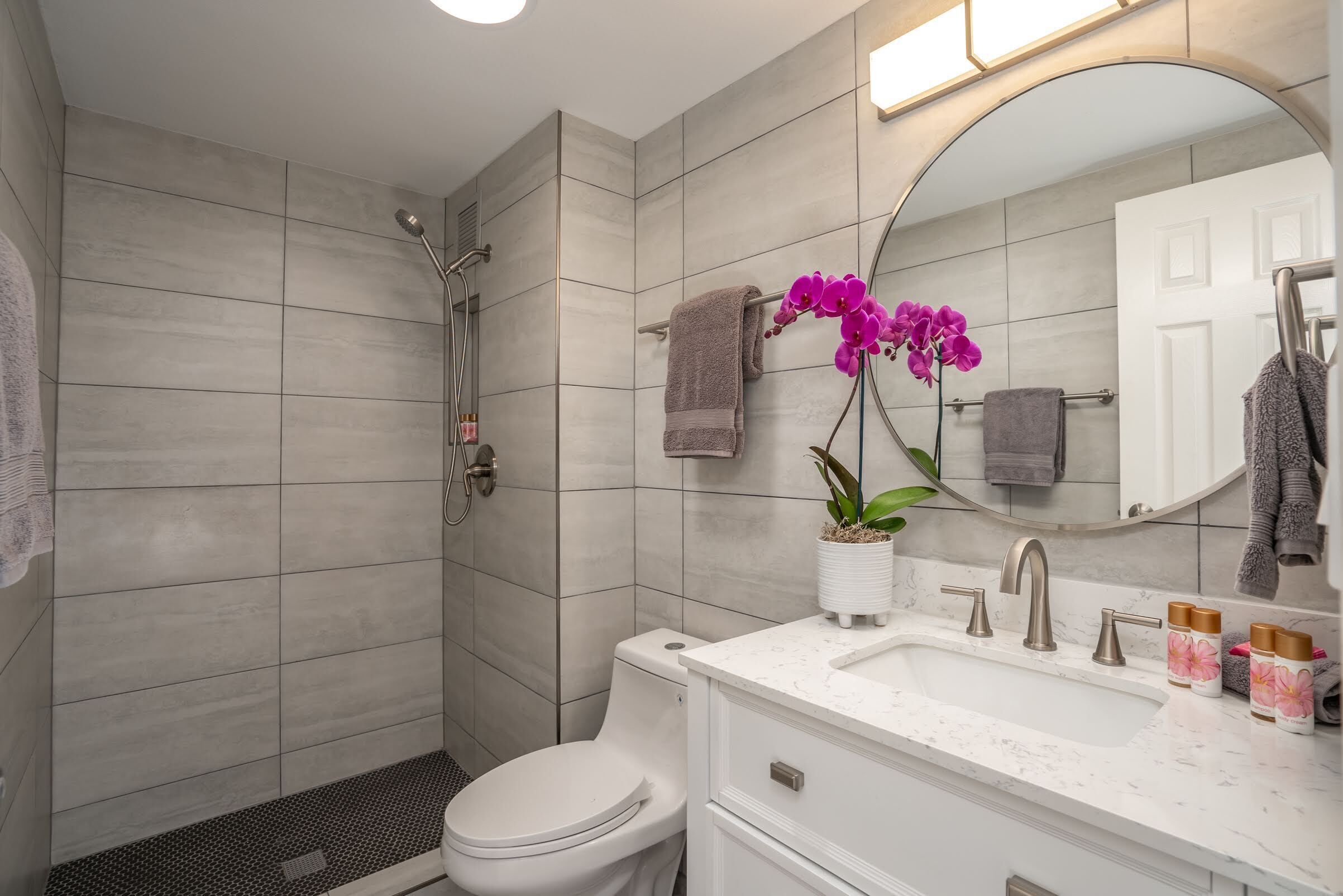 Een moderne badkamer met douche, toilet, wastafel en een grote spiegel.