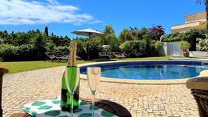 A poolside area with a table set for two, a bottle of champagne, and a glass of champagne. - Albufeira Balaia Villa With Private Pool (Albufeira)