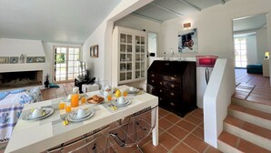 A spacious living area with a dining table set for breakfast, a fireplace, and a large cabinet. - Albufeira Balaia Villa With Private Pool (Albufeira)