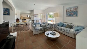 A spacious living room with a dining area, a kitchen in the background, and a view of the outdoors. - Albufeira Balaia Villa With Private Pool (Albufeira)