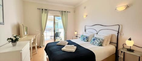 Ein Hotelzimmer mit Bett, Nachttischen, einem Schreibtisch, einem Stuhl und Blick auf den Balkon.