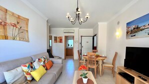 Een moderne woonkamer met een bank, salontafel, eettafel en televisie.