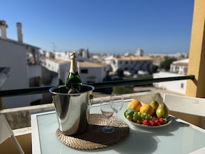 A balcony with a table set for a meal, featuring a bottle of champagne, wine glasses, and a plate of fruit. - Quarteira Classic With Pool by Homing (Loulé)