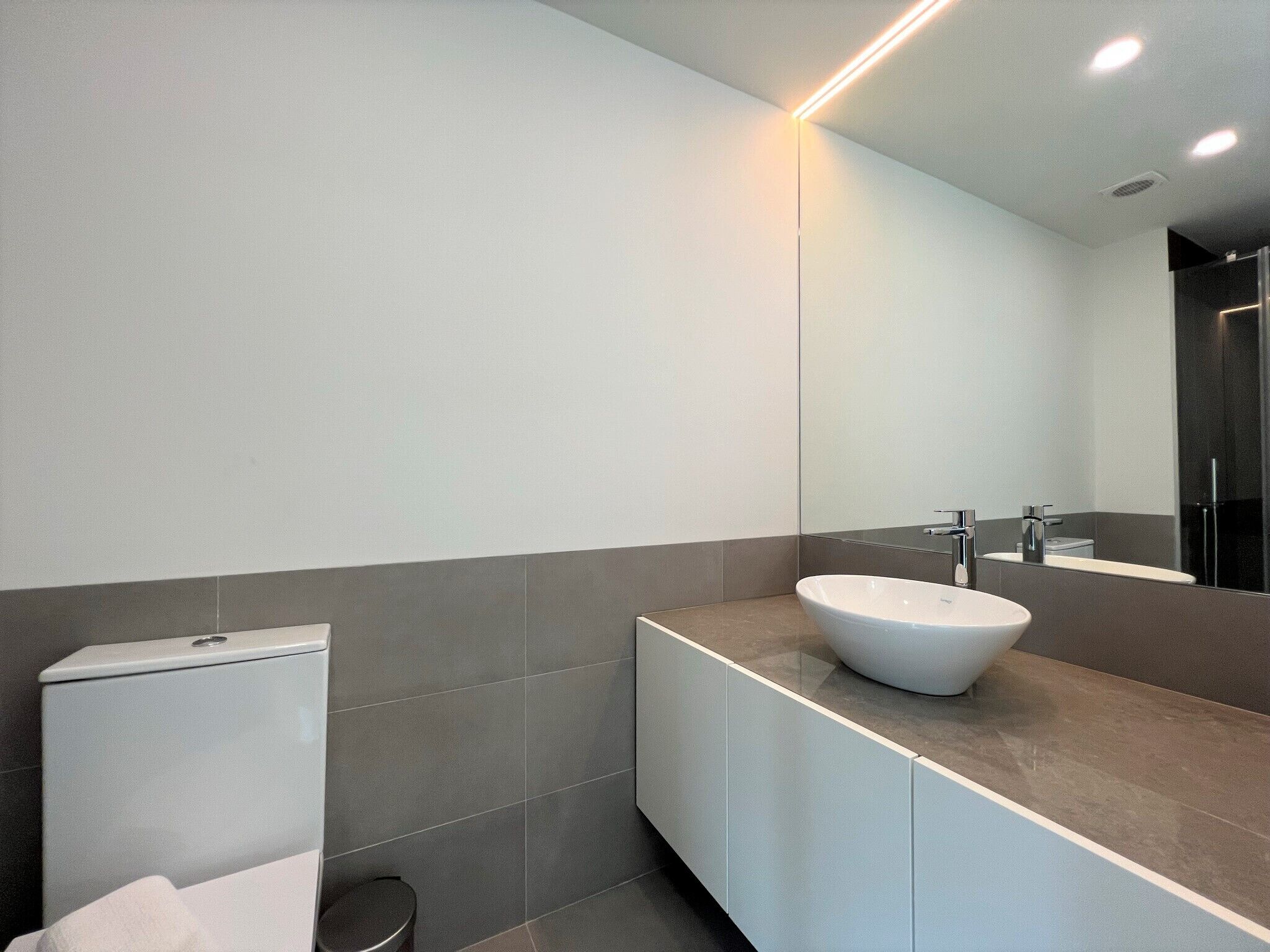A modern bathroom with a white sink, a toilet, and a mirror.