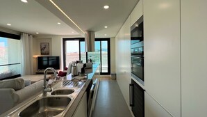 A modern kitchen with a central island, stainless steel appliances, and a large window providing a view of the city. - Faro Design 2 by Homing (Faro)