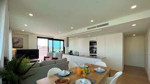 A modern living room with a sofa, a dining table set for breakfast, and a kitchen area with a microwave and sink. - Faro Design 2 by Homing (Faro)
