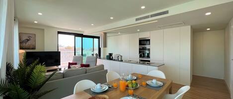 A modern living room with a sofa, a dining table set for breakfast, and a kitchen area with a microwave and sink.