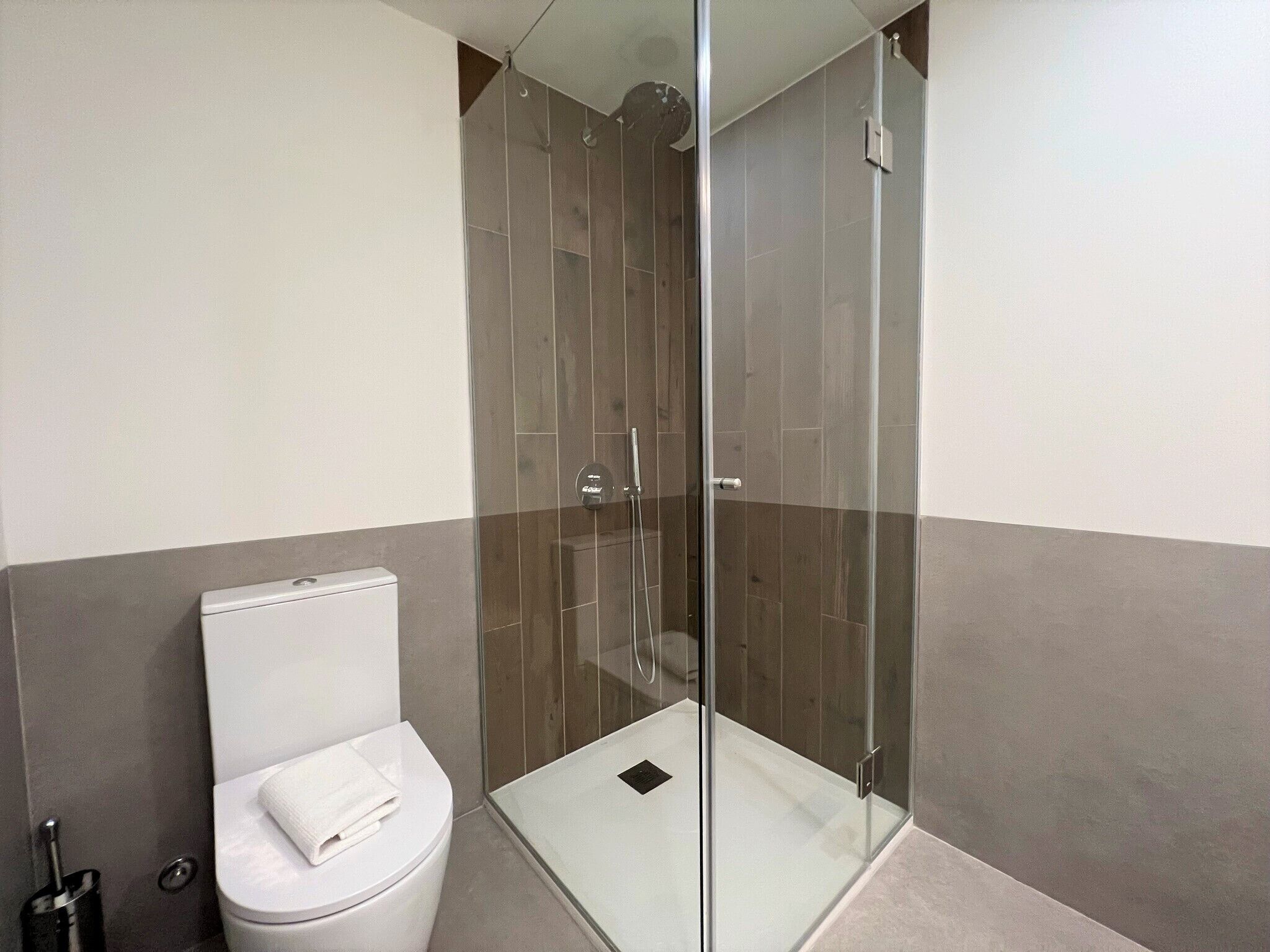 A modern bathroom with a glass-enclosed shower, a white toilet, and a towel on the seat.