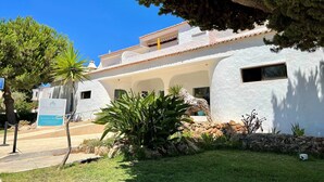 A white building with a tiled roof, a stone wall, and a grassy area with plants. - Armação DE Pêra Twins 1 With Pool (Lagoa)