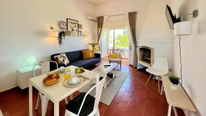A modern living room with a sofa, dining table, and fireplace. There is a balcony with a view of the outdoors. - Armação DE Pêra Twins 1 With Pool (Lagoa)