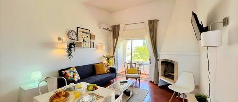 Una sala de estar moderna con sofá, mesa de comedor y chimenea. Cuenta con un balcón con vistas al exterior.