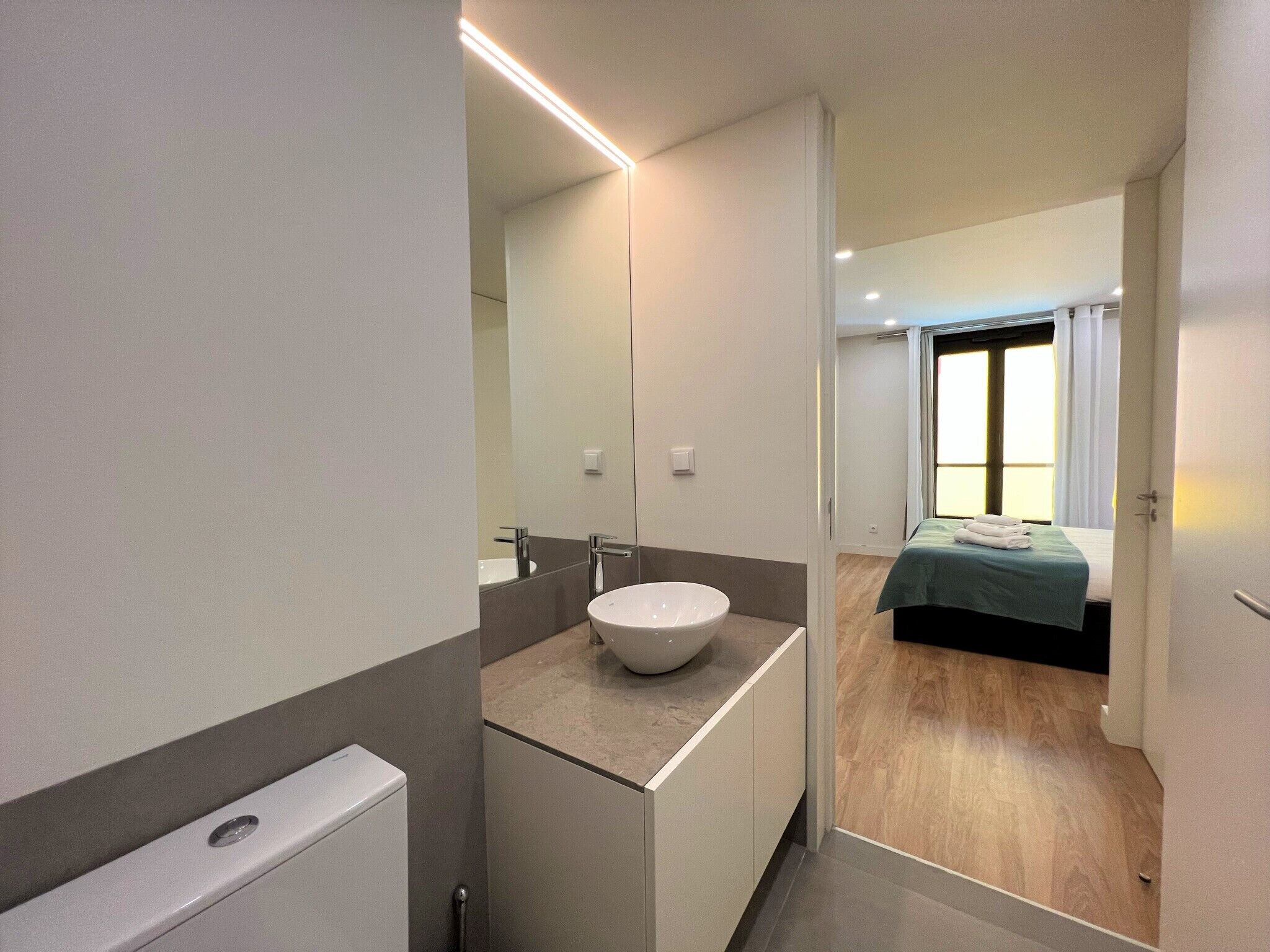 A modern bathroom with a large mirror, a white sink, and a toilet.