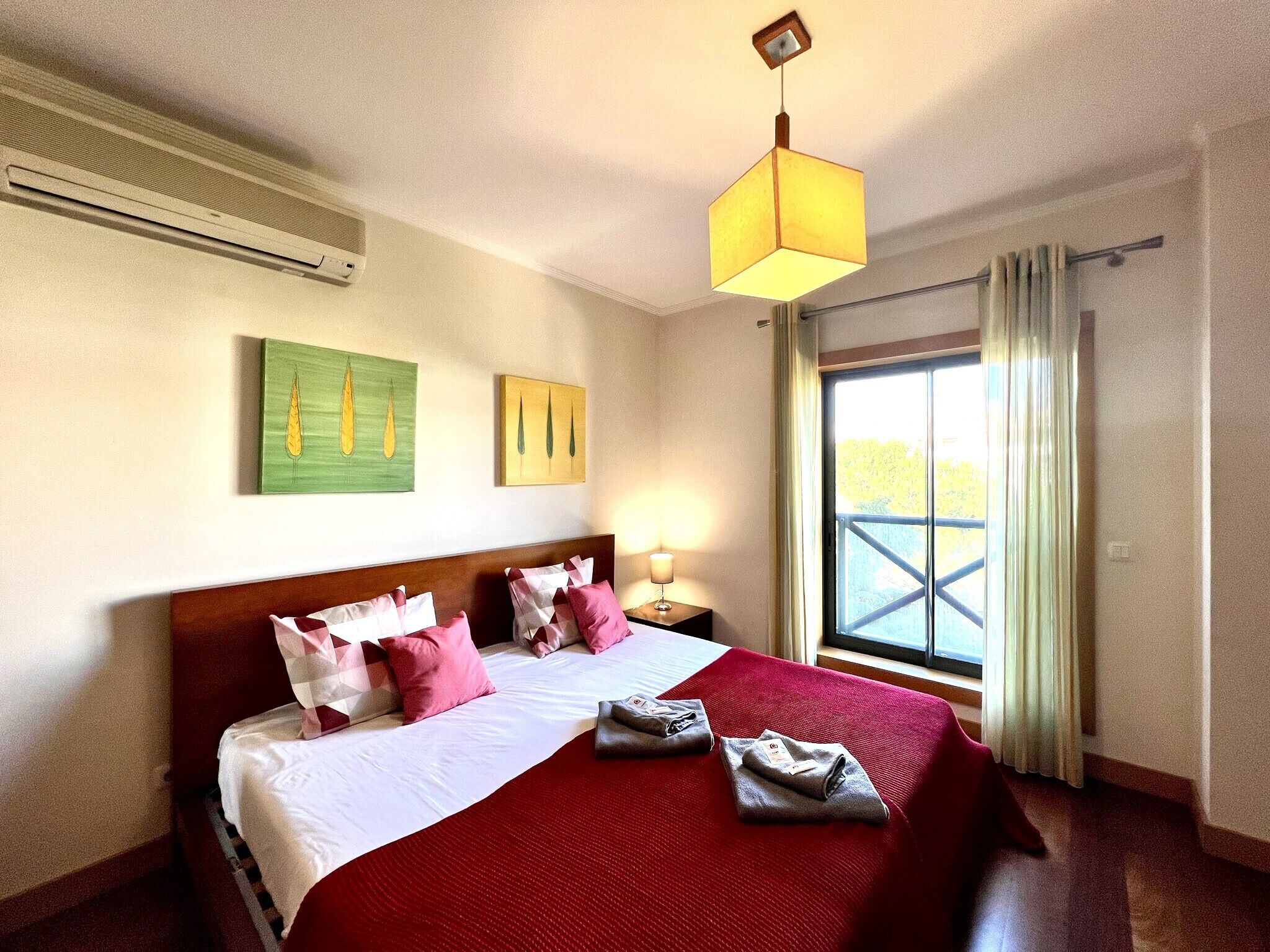 A hotel room with a bed, a nightstand, a lamp, and a window with curtains.