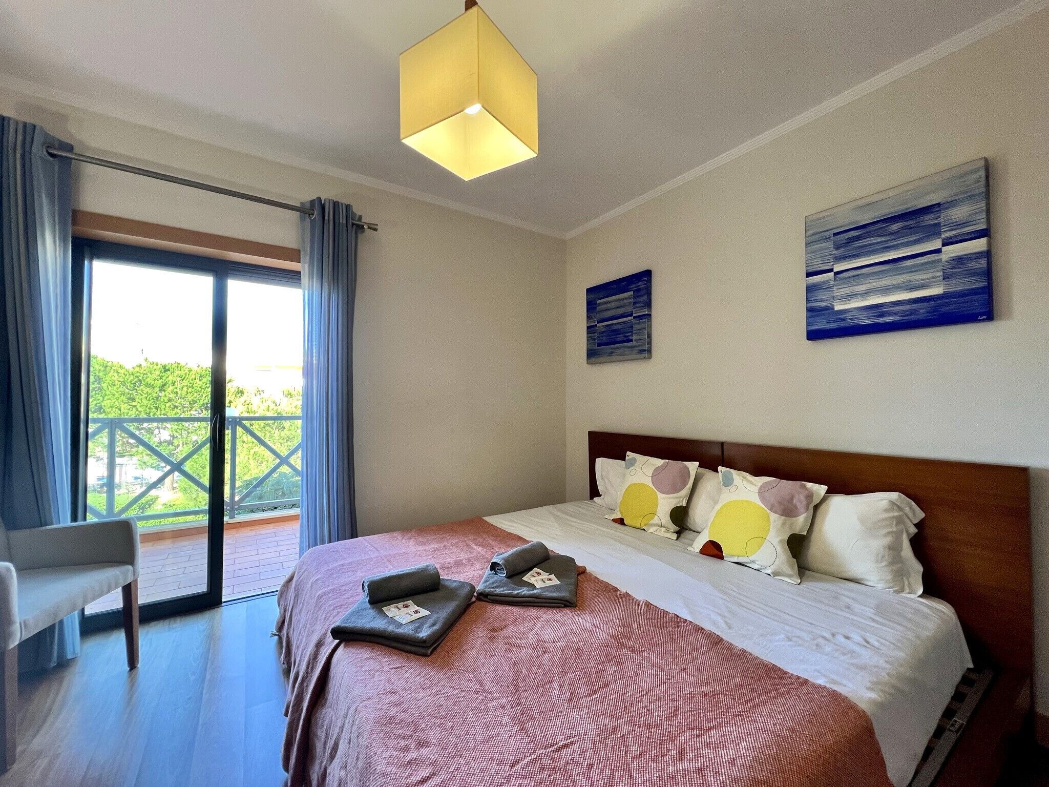 Ein Hotelzimmer mit Bett, Sessel, Balkon und zwei Bildern an der Wand.