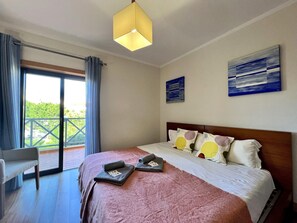 A hotel room with a bed, a chair, a balcony, and two paintings on the wall. - Albufeira Modern 3 With Pool by Homing (Albufeira)