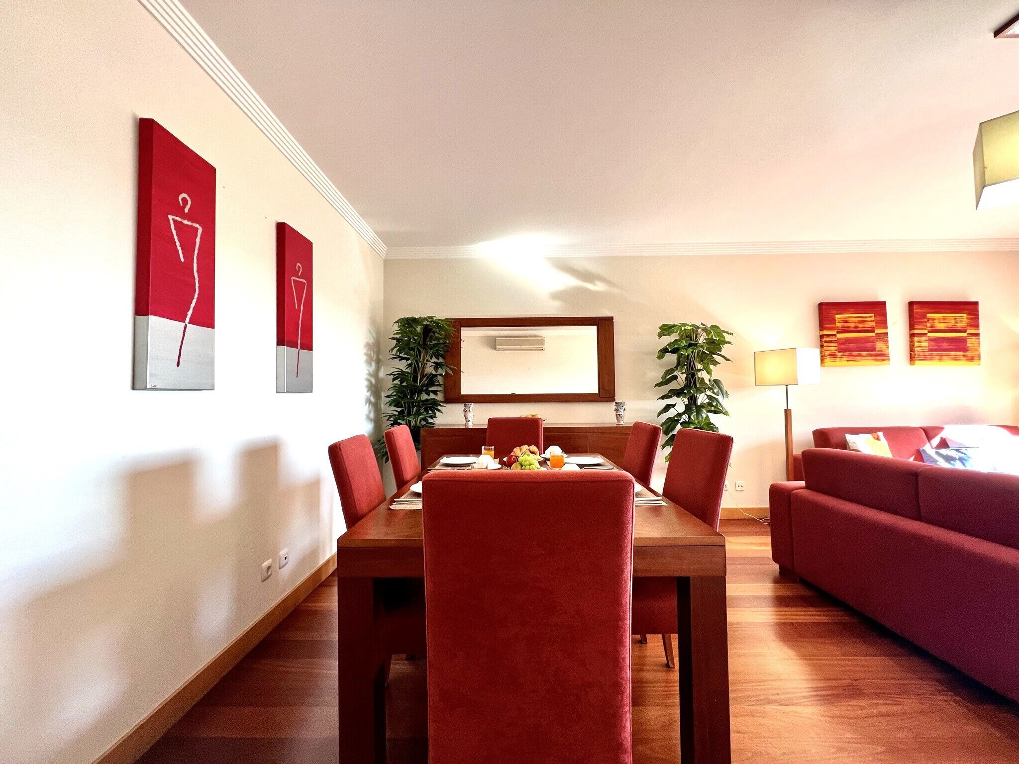 Un comedor moderno con una mesa de madera y sillas tapizadas de rojo, flanqueado por sofás rojos y un espejo grande.