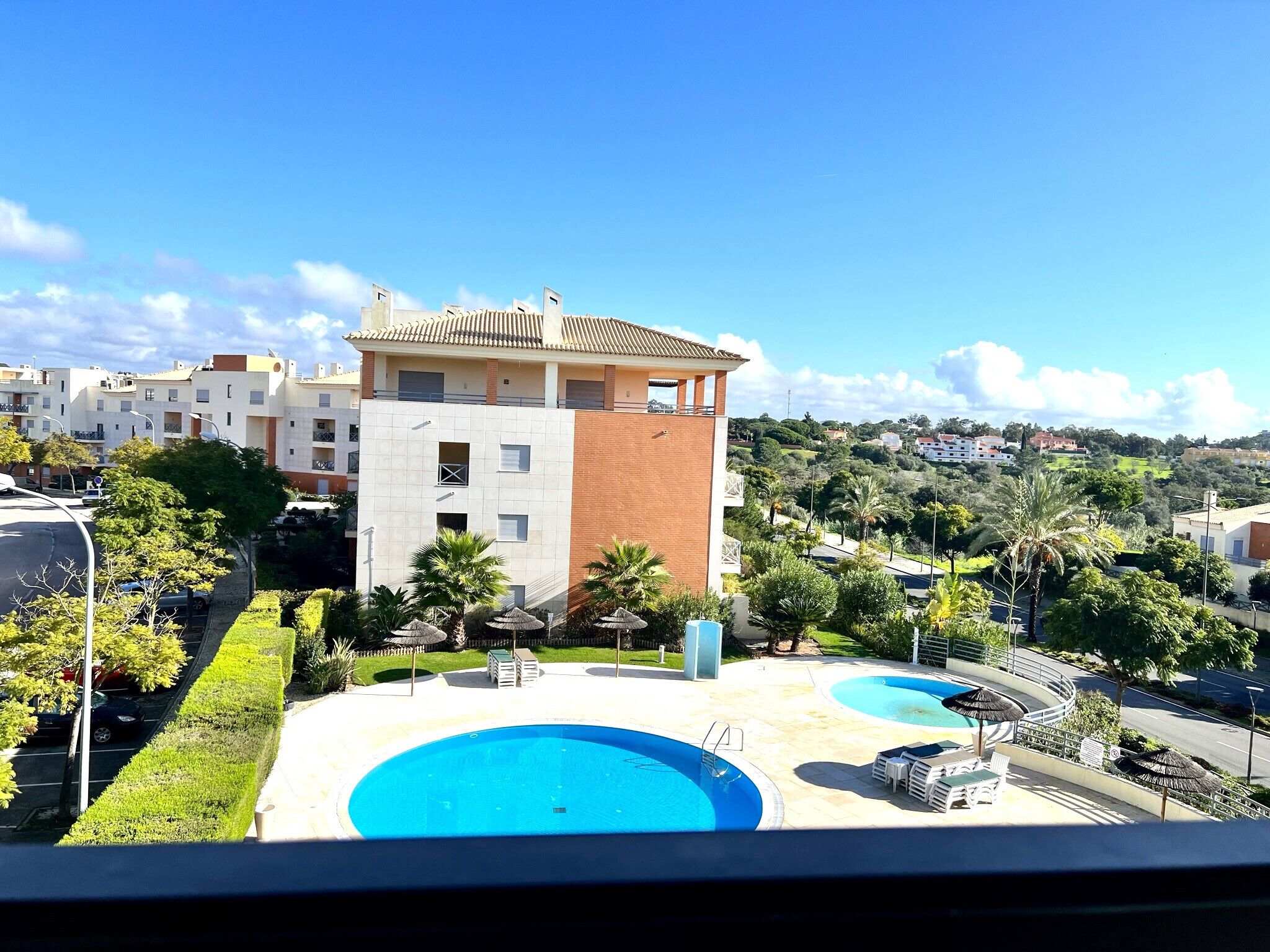 A modern building with a rooftop terrace, a swimming pool, and a view of a residential area.