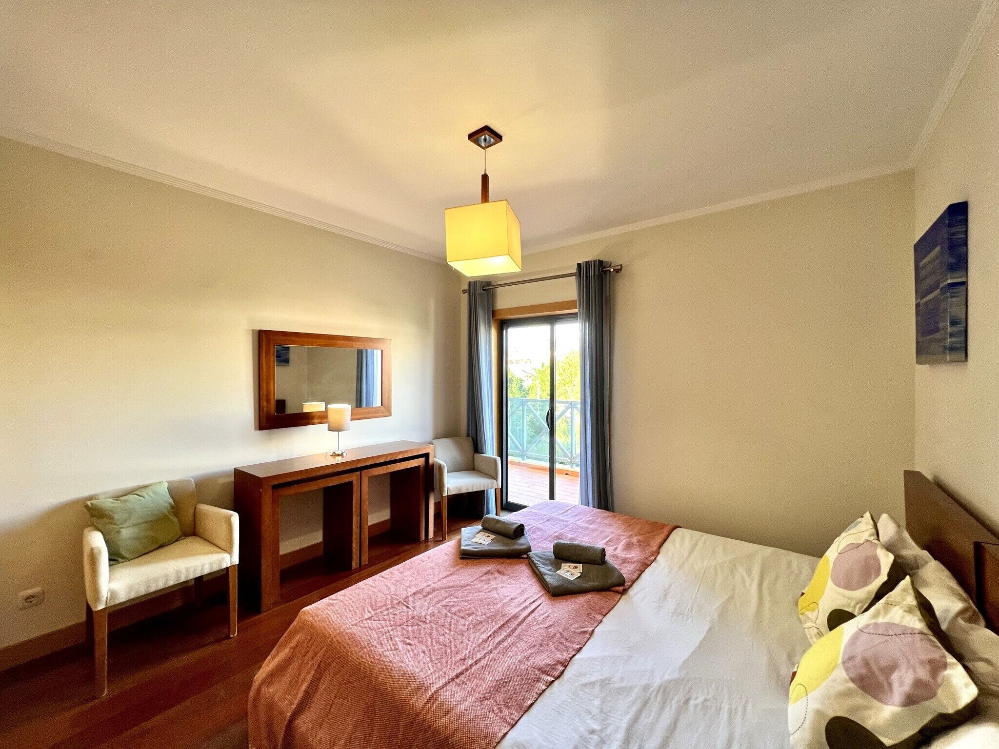 A hotel room with a bed, a desk, a chair, a mirror, and a window with curtains.