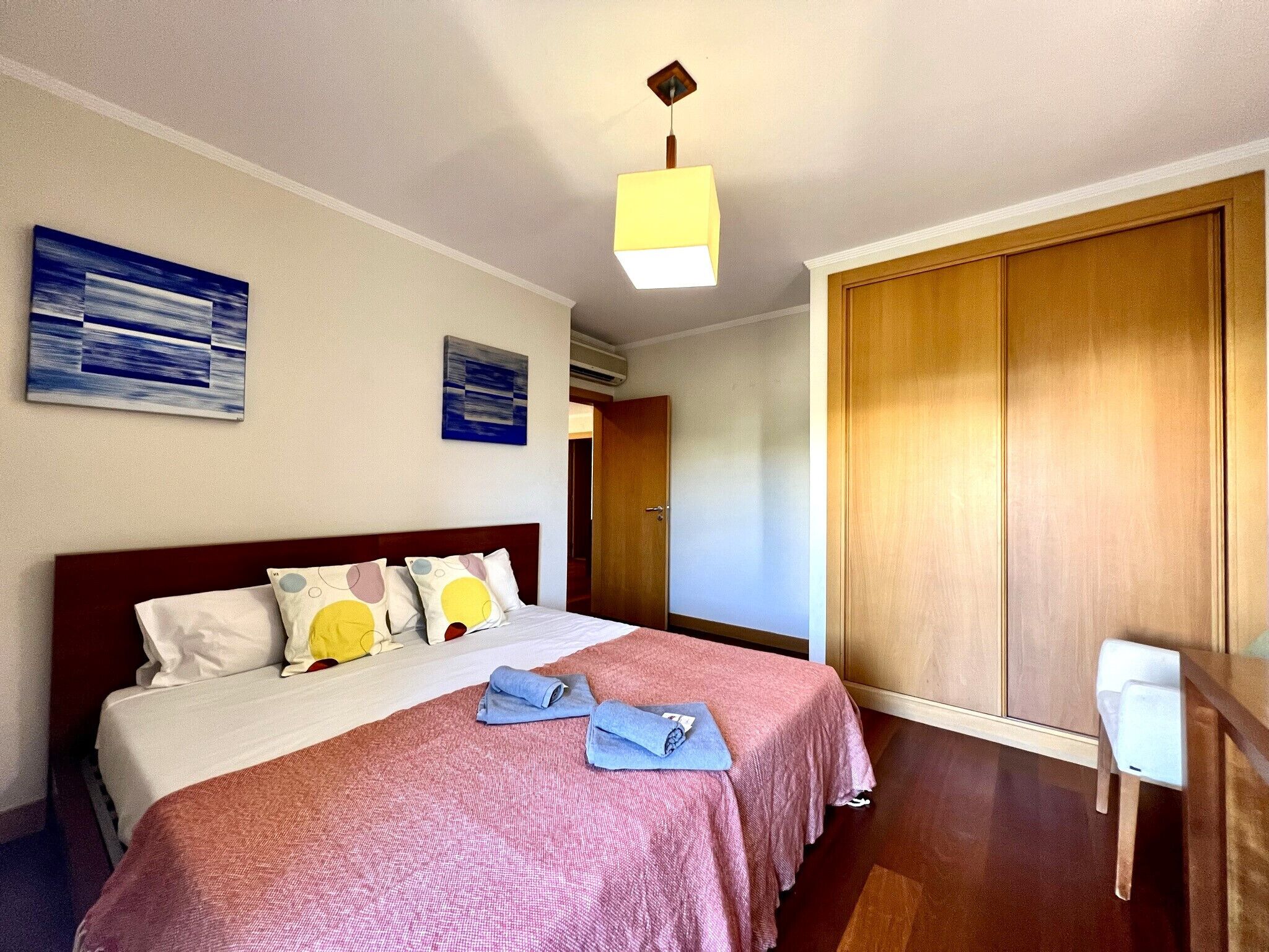 A hotel room with a bed, two pillows, a bedside table, a lamp, and a wardrobe.