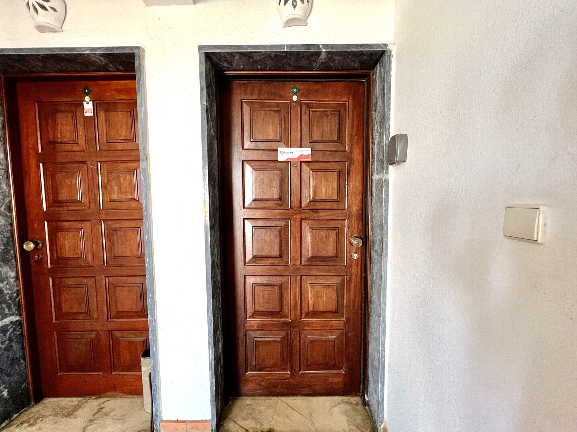 Two wooden doors with a marble threshold, a light switch, and a small sign on the right door.