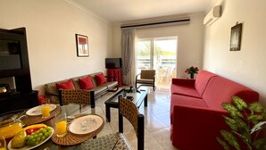 A living room with a red sofa, patterned sofa, dining table with placemats, and a TV on a stand. - Vilamoura Typical 2 With Pool by Homing (Loulé)