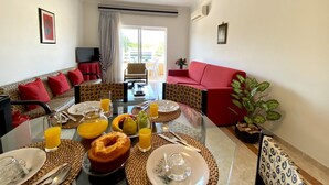 A dining area with a glass table set for breakfast, including plates, cutlery, and a variety of fruits and juices. - Vilamoura Typical 2 With Pool by Homing (Loulé)