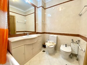 Een moderne badkamer met een wastafel, toilet, bidet en een grote spiegel.