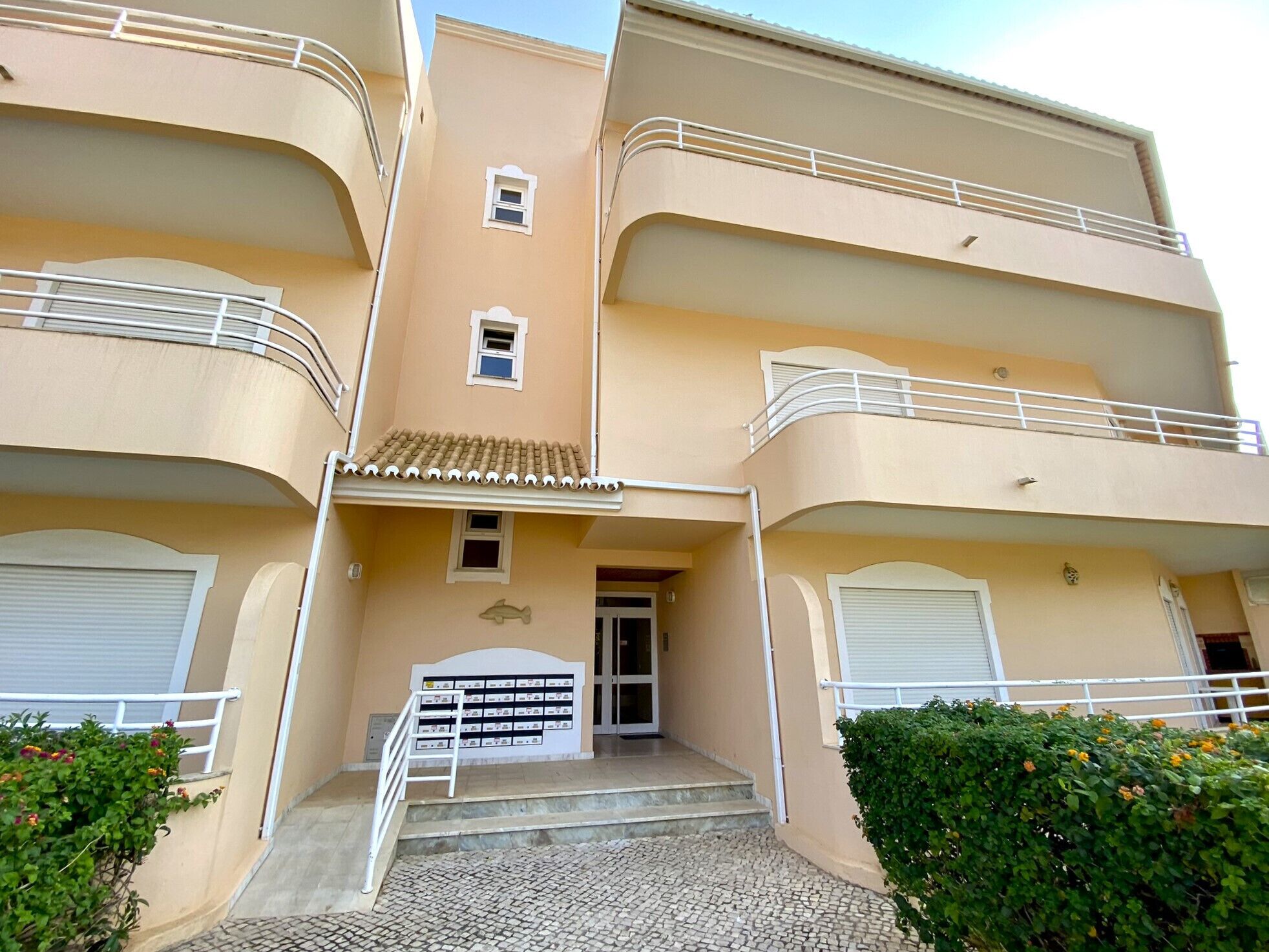 A multi-story building with balconies, a tiled entrance, and a small window.