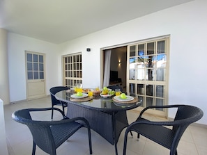 A dining area with a round table and four chairs, a door, and a window with curtains. - Vilamoura Garden View 2 With Pool (Loulé)