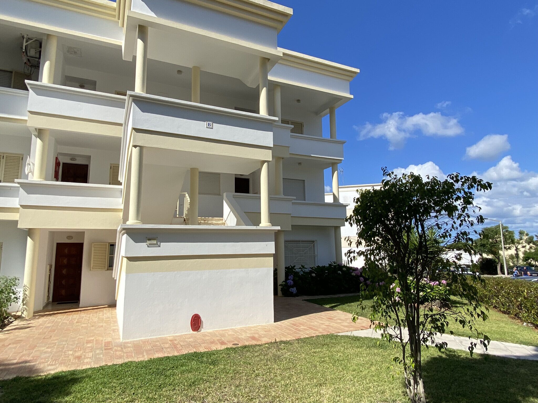A multi-story residential building with balconies, a red fire hydrant, and a well-maintained lawn.