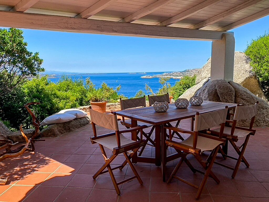 A wooden table and chairs set outdoors with a view of the sea.