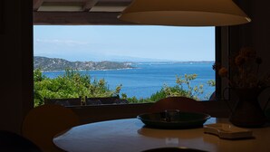 Una mesa con una lámpara, un cuenco y un florero con flores, con vistas a la costa, vegetación y montañas.