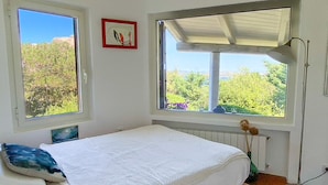Un dormitorio con una cama, dos ventanas, un radiador y una lámpara de pie.