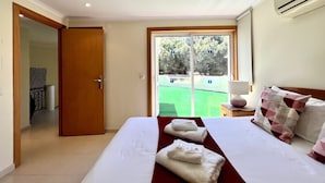 A hotel room with a bed, a window with a view of a tennis court, a door, and an air conditioning unit. - Vilamoura Amazing Golf Villa With Pool (Loulé)